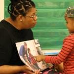 A teacher and preschool student read a book together.